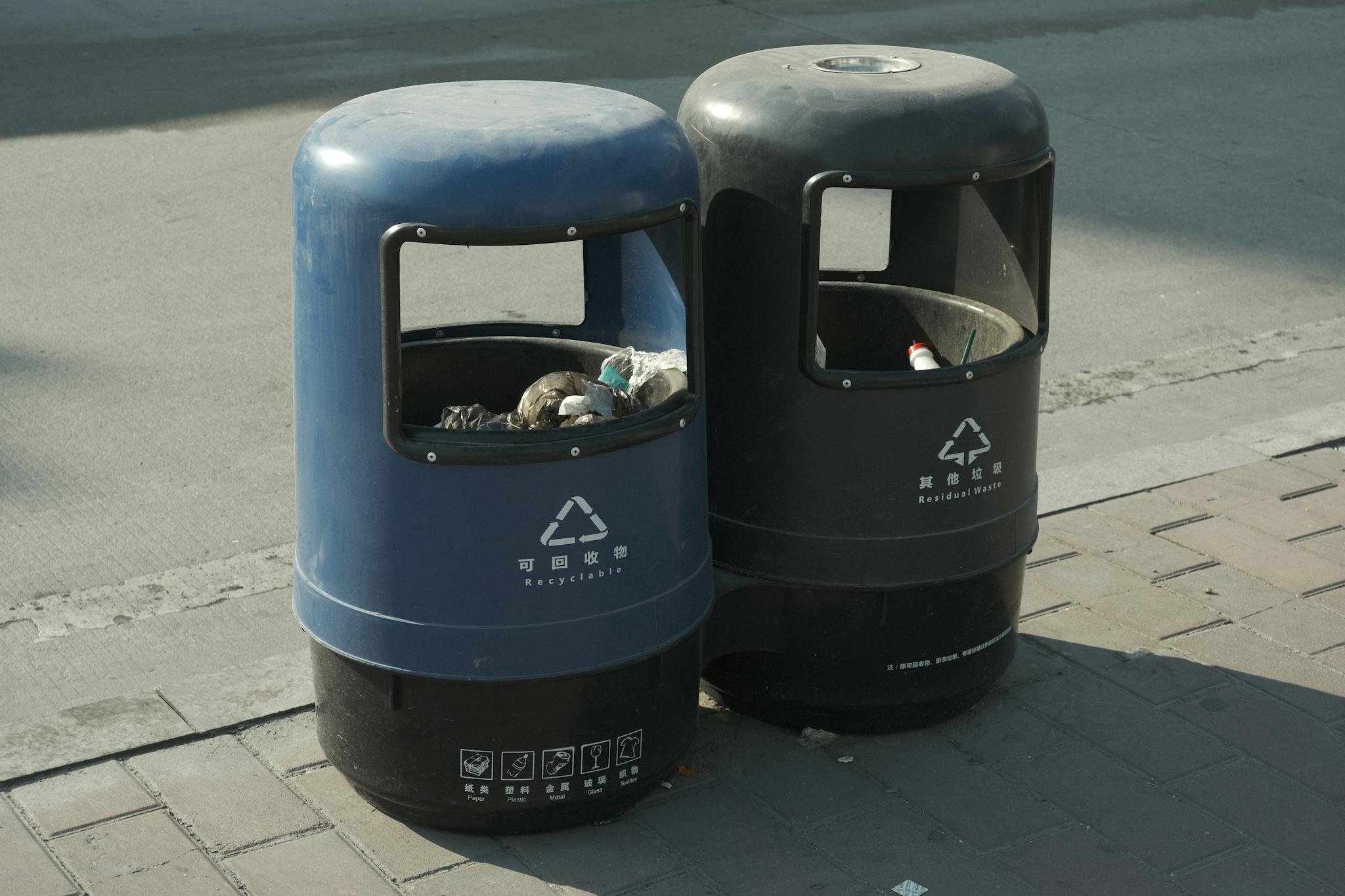 Blue and black recycling and waste bins on a city sidewalk, emphasizing urban waste management.